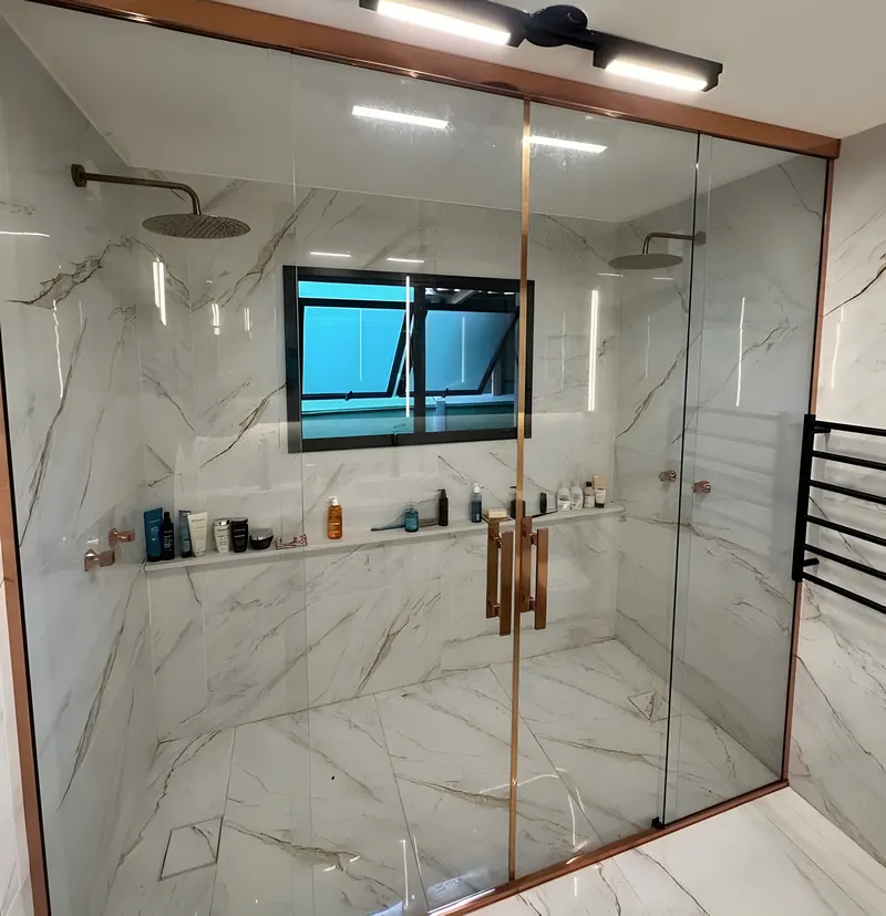 Box de vidro do piso ao teto com perfil rosé em banheiro de mármore