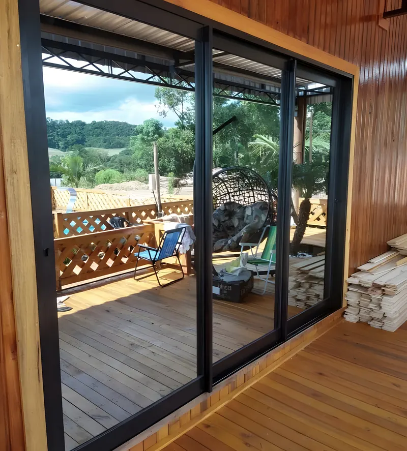 Porta de vidro de correr com perfil preto abrindo para um deck de madeira